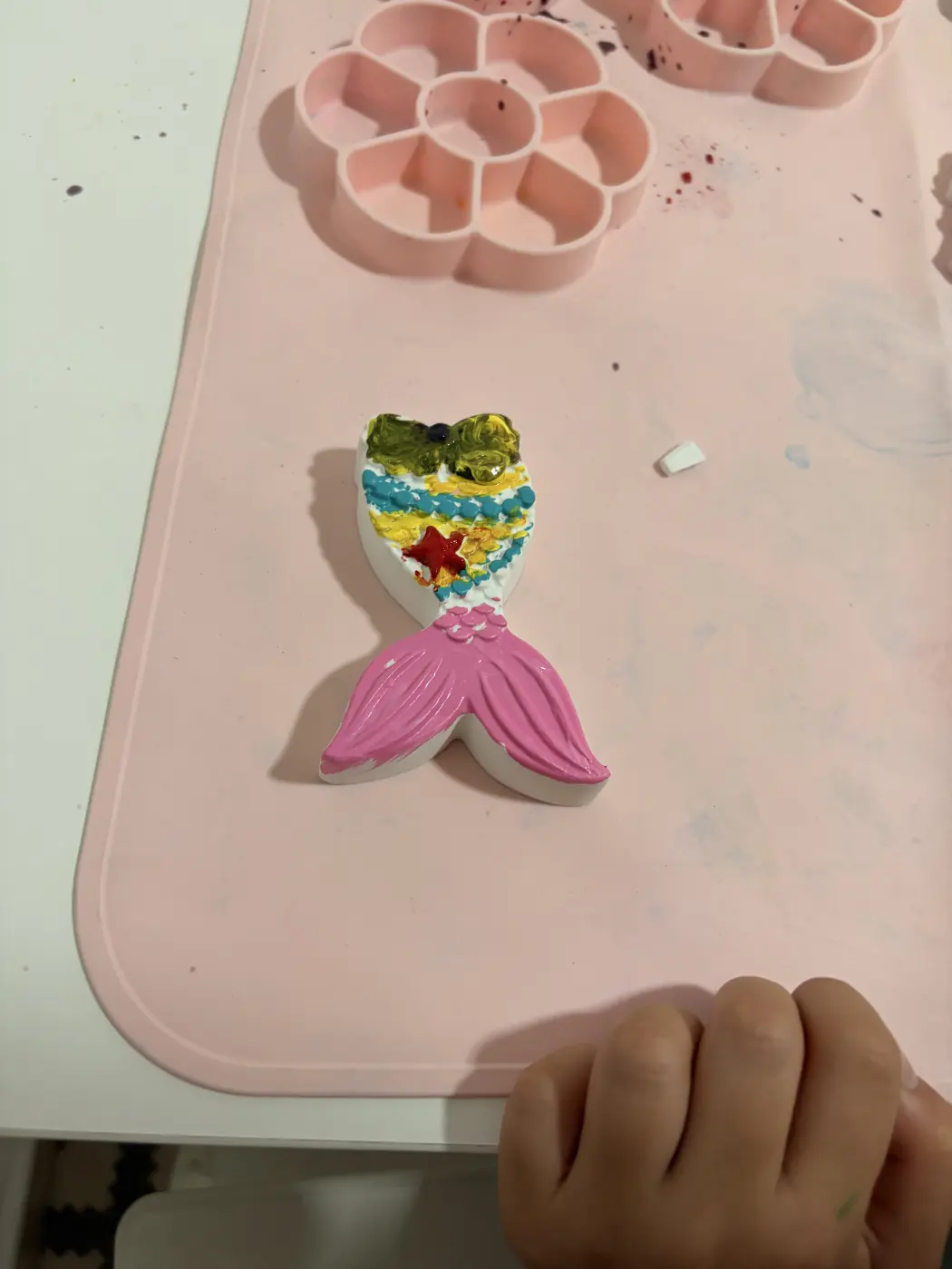 Painted plaster mermaid with a bright pink tail and colourful details on a pink craft mat.