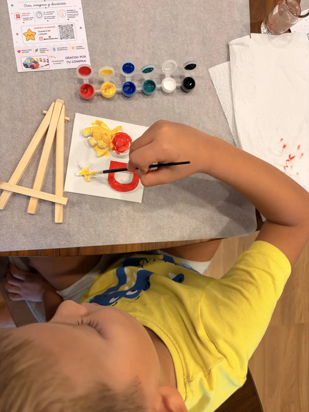 A child paints a yellow astronaut, red letter D and star on a small canvas using the Mini Makers paint set.