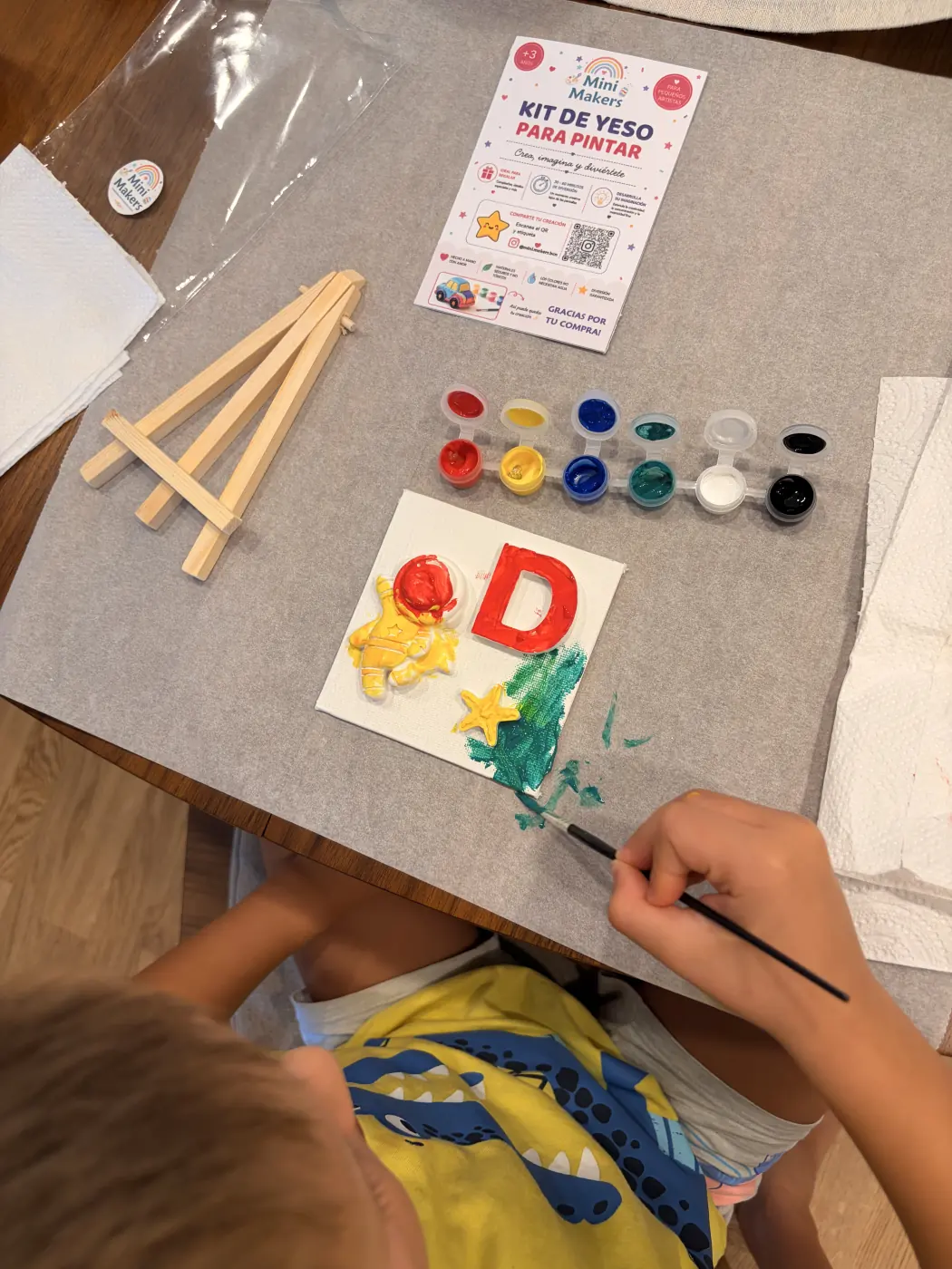 A child paints the teal background around a yellow astronaut, red letter D and yellow star.